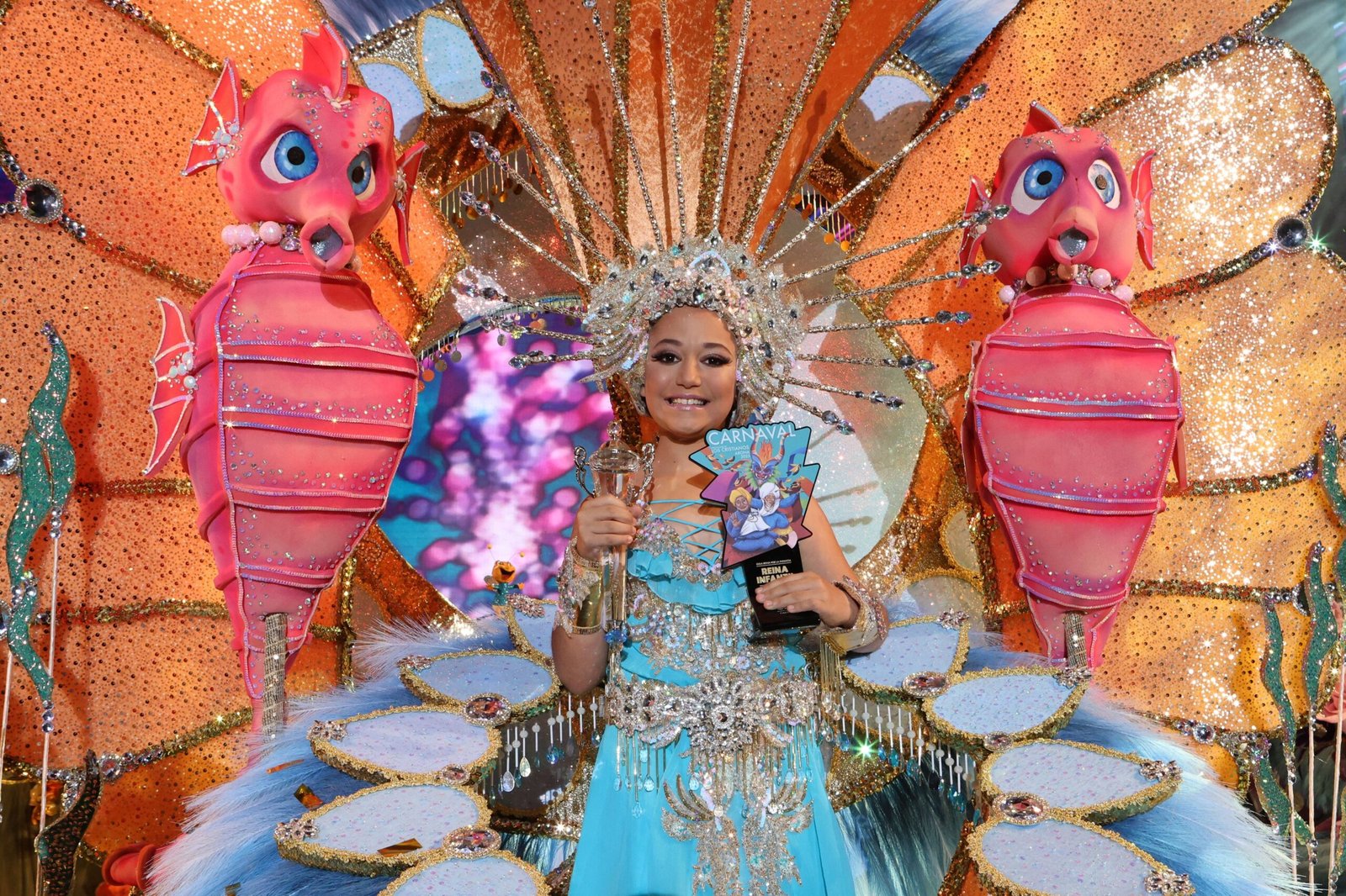 Ariadna Cabrera Almenara, coronada Reina por la Infancia del Carnaval Internacional de Los Cristianos 2025
La nueva reina, que lució la fantasía ‘Agua’ de Dani Mesa, tiene como séquito real a Gisela Aguilar Felipe, Dayara Araujo Muñoz, Valeria Hernández Rodríguez y Ayleen Acosa Reyes.
Ariadna Cabrera Almenara, representando a Yaiza Nueva Línea, Restaurante La Marina y Peluquería M&C, fue coronada Reina por la Infancia del Carnaval Internacional de Los Cristianos 2025 en una emocionante Gala de Elección que contó con la presencia de cinco candidatas. Luciendo la fantasía ‘Agua’ obra del diseñador Dani Mena, Ariadna Cabrera recibió el cetro de manos de la alcaldesa de Arona, Fátima Lemes; y el concejal de Fiestas, Alexis Gómez, en presencia de la Reina de la pasada edición, Daniela Ramallo Arzola. También estuvo presente Dafne Mendoza González, que hace pocas semanas se proclamó Cuarta Dama infantil del Carnaval de Santa Cruz.
El séquito real lo formaron como Primera Dama de Honor Gisela Aguilar Felipe, quien lució la fantasía ‘Atardecer en el Llano’, obra del diseñador Alfonso Baute con el patrocinio de La Cueva de Paco El Campesino, Tizón Imprenta, Mundiópticas Los Abrigos, Guachinche La Maestra y Transportes DTS; Dayara Araujo Muñoz fue nombrada Segunda Dama de Honor. Vistió la fantasía ‘Mua-Mua-Plaf’ obra de la diseñadora Silvia María Ferrera Pérez con el patrocinio de Comparsa Infantil Playeritos, Comparsa Ritmo Sureño y Monkey Painters. Valeria Hernández Rodríguez lució la fantasía ‘La Tierra de mis Abuelos’ obra del diseñador Jean Pierre Rosales con el patrocinio de Taller Victoria S.L y Viveros La Cosma; y Ayleen Acosta Reyes llevó la fantasía ‘El Sueño de Ayleen’ obra de la diseñadora Nieves Ramos con el patrocinio de Nuevo Stylo Sur, Venus Salón de Belleza Unisex, Club Hipico Del Sur y Floristeria Manoly.
Todas las candidatas recibieron, además, una entrada doble a Jungle Park y a Aqualand gentileza de Aspro Ocio; y un kit de material escolar gentileza de Folder. La elección de la Reina de la Infancia llenó el Recinto del Carnaval en el Bulevar Chajofe de Los Cristianos. La Gala, que contó con la dirección de Amabelys Cartagena, contó con la participación del Ballet Banky, que en su actuación rindió homenaje a Venezuela -el tema central del Carnaval aronero de este 2025-; la Escuela de Gimnasia Rítmica de Arona, que actuó bajo la dirección y coreografía de Silvia Ferrera luciendo la fantasía ‘Mi linda Venezuela otra vez’; los 74 alumnos de los Grupos Infantiles Coreográficos del Patronato de Cultura de Arona, dirigidos por Naím Yánez Alonso, con la fantasía ‘Ecos de África Tribal’ de la diseñadora María Victoria Alcaide, quienes interpretaron una coreografía de Laly Cruz que contó con los arreglos musicales de Alba Hernández; y la actuación estrella de Rafael Flores El Morocho, autor de la Canción del Carnaval, que interpretó un mix con las mejores canciones infantiles de todos los tiempos.