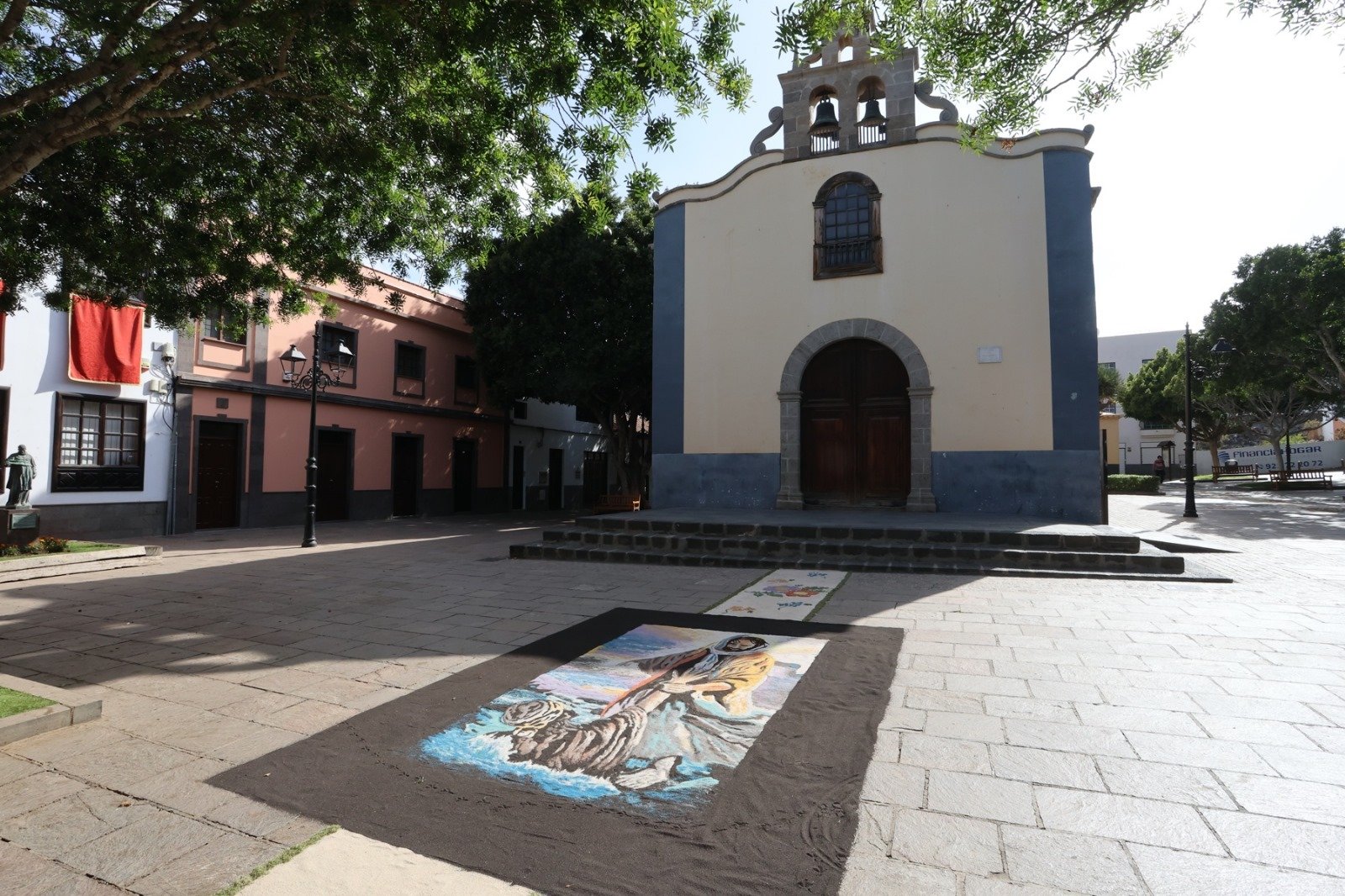 Arona se llenará de alfombras tradicionales para la celebración del Corpus Christi

El casco histórico de Arona, junto con los núcleos de Valle San Lorenzo, Buzanada, La Camella, Cabo Blanco, Las Galletas, Guargacho, El Fraile y Parque La Reina, se unirán en la confección de estos tapices multicolores.

Las calles del municipio de Arona volverán a llenarse de color, tradición y fervor con la celebración del Corpus Christi, una de las festividades religiosas más arraigadas en la cultura local. Durante el fin de semana del 21 y 22 de junio, vecinos y feligreses de todos los núcleos del municipio se volcarán en la elaboración de alfombras artesanales, una expresión de arte efímero que adorna el paso del Santísimo Sacramento durante las procesiones.

Uno de los principales puntos de encuentro será el casco histórico de Arona, donde la comunidad de la Parroquia San Antonio Abad dará inicio a la confección de alfombras la noche del sábado 21 de junio, a partir de las 21:30 horas. Durante toda la madrugada y hasta el mediodía del domingo, la Plaza del Santísimo Cristo de la Salud y las calles El Calvario, Domínguez Alfonso, La Luna y Duque de la Torre se transformarán en un tapiz multicolor, elaborado con paciencia y dedicación por grupos vecinales, familias y colectivos parroquiales.

El domingo 22 de junio, a las 19:30 horas, se celebrará la solemne Eucaristía en el templo de San Antonio Abad. A continuación, a las 20:15 horas, dará comienzo la procesión del Corpus Christi, en la que el Santísimo Sacramento recorrerá las calles decoradas, acompañado por la Banda de Música de Arona y una nutrida representación de la comunidad.

Pero no solo el casco de Arona vivirá con intensidad esta festividad. También en los núcleos de Valle San Lorenzo, Buzanada, La Camella, Cabo Blanco, Las Galletas, Guargacho, El Fraile y Parque La Reina, las parroquias han preparado una programación especial que incluye la confección de alfombras y procesiones solemnes.

Desde la tarde del sábado, los vecinos comenzarán a crear estos delicados trabajos florales que, más allá de su belleza artística, son un acto de fe y una muestra de identidad cultural.

En lugares como Valle San Lorenzo y La Camella, las alfombras comenzarán a elaborarse desde las 16:00 horas del sábado, mientras que, en Cabo Blanco, El Fraile o Las Galletas, los trabajos comenzarán a primera hora del domingo.

Esta manifestación popular, que combina religiosidad y arte popular, se ha convertido en una de las tradiciones más esperadas del calendario litúrgico del municipio.